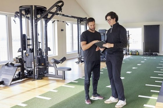 Ein junger Mann und ein Fitnesstrainer erstellen am Tablet einen Trainingsplan.